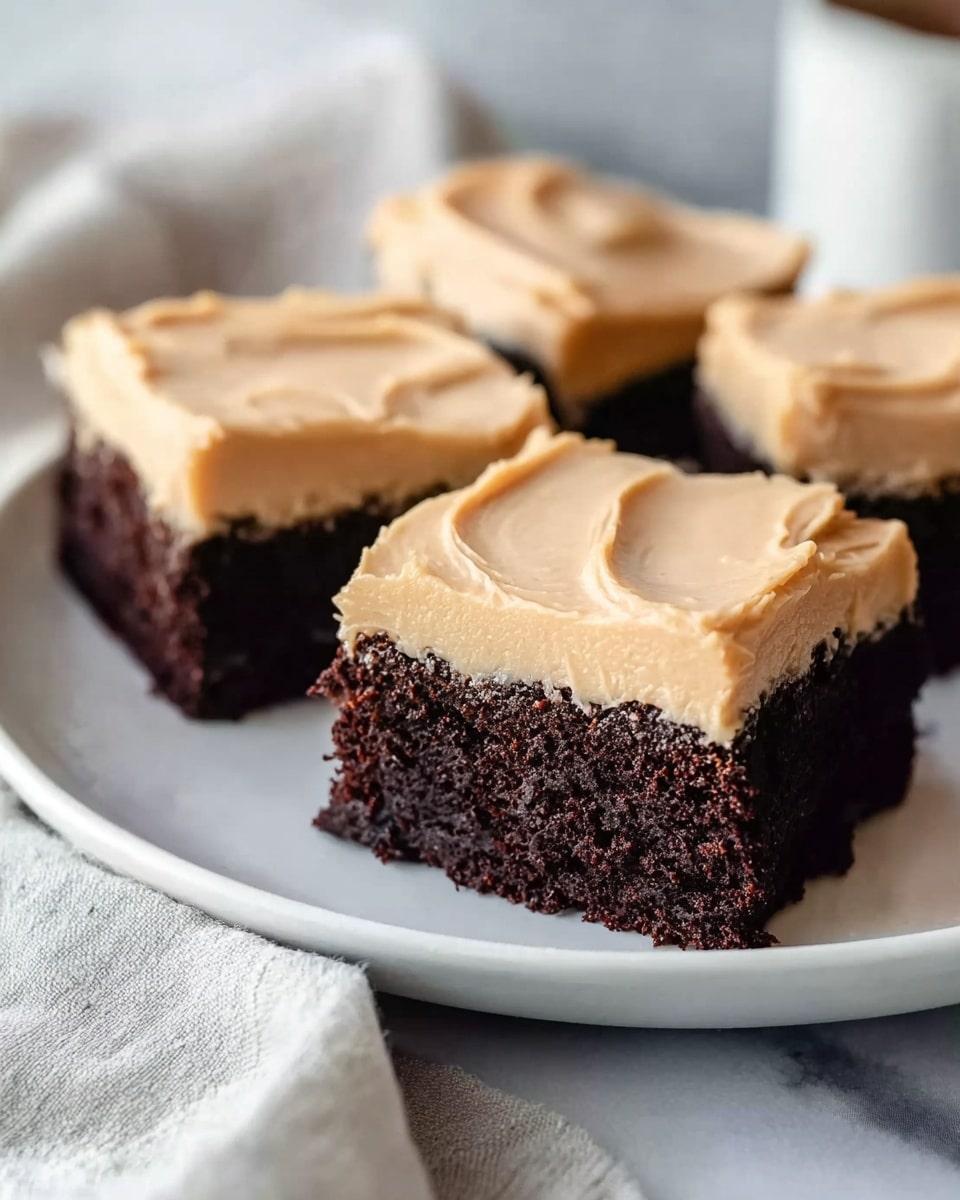 Three square pieces of chocolate cake with a thick layer of light tan frosting on top, each piece showing a dense, moist, dark brown cake base and a smooth, creamy frosting layer with soft swirled texture. The pieces are arranged closely on a white plate resting on a white marbled surface. The background is softly blurred with warm tones. Photo taken with an iphone --ar 4:5 --v 7