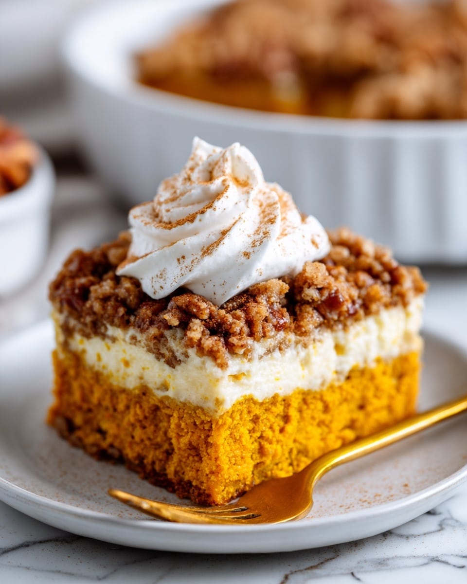 A close-up of a slice of pumpkin cake on a white plate with a gold fork beside it. The cake has three layers: a dense orange pumpkin base, a creamy white middle layer, and a crumbly brown topping with pecan pieces scattered on top. A swirl of white whipped cream sits on top of the crumble, sprinkled with a small amount of cinnamon powder. The background is a white marbled surface with a blurred pie dish filled with the same cake in the distance. Photo taken with an iphone --ar 4:5 --v 7