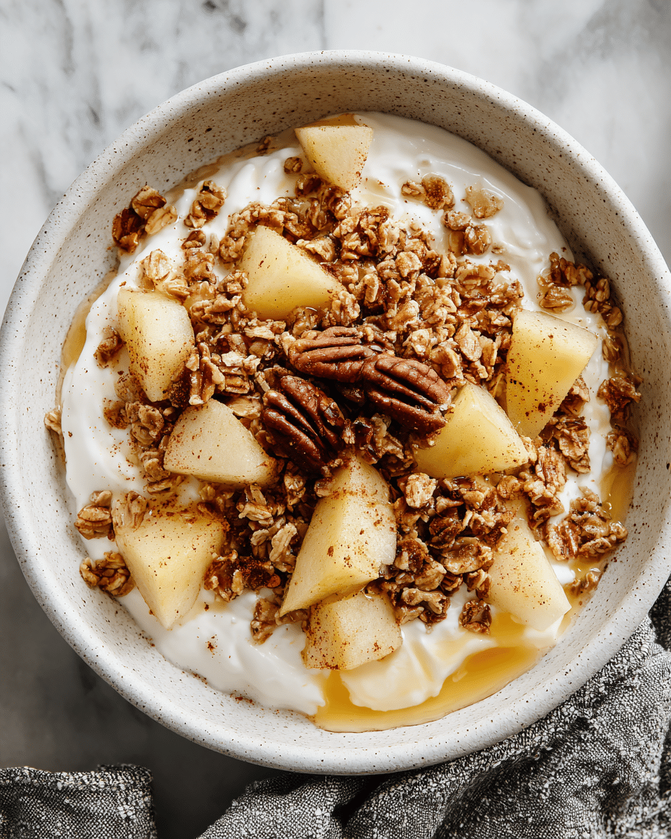 A white speckled bowl filled with a creamy white cottage cheese base, topped with small clusters of golden brown granola spread unevenly over the surface. On top of the granola, light yellow pear chunks are scattered, some slightly overlapping. In the center, a small pile of dark brown pecans adds texture and color contrast. A light drizzle of amber honey pools around the fruit and nuts, glistening and adding a sticky sheen. The whole dish is sprinkled lightly with a fine dusting of cinnamon, visible as a soft brown powder over the pears and granola. The bowl sits on a white marbled surface, with a grey textured cloth partially seen behind it. photo taken with an iphone --ar 4:5 --v 7