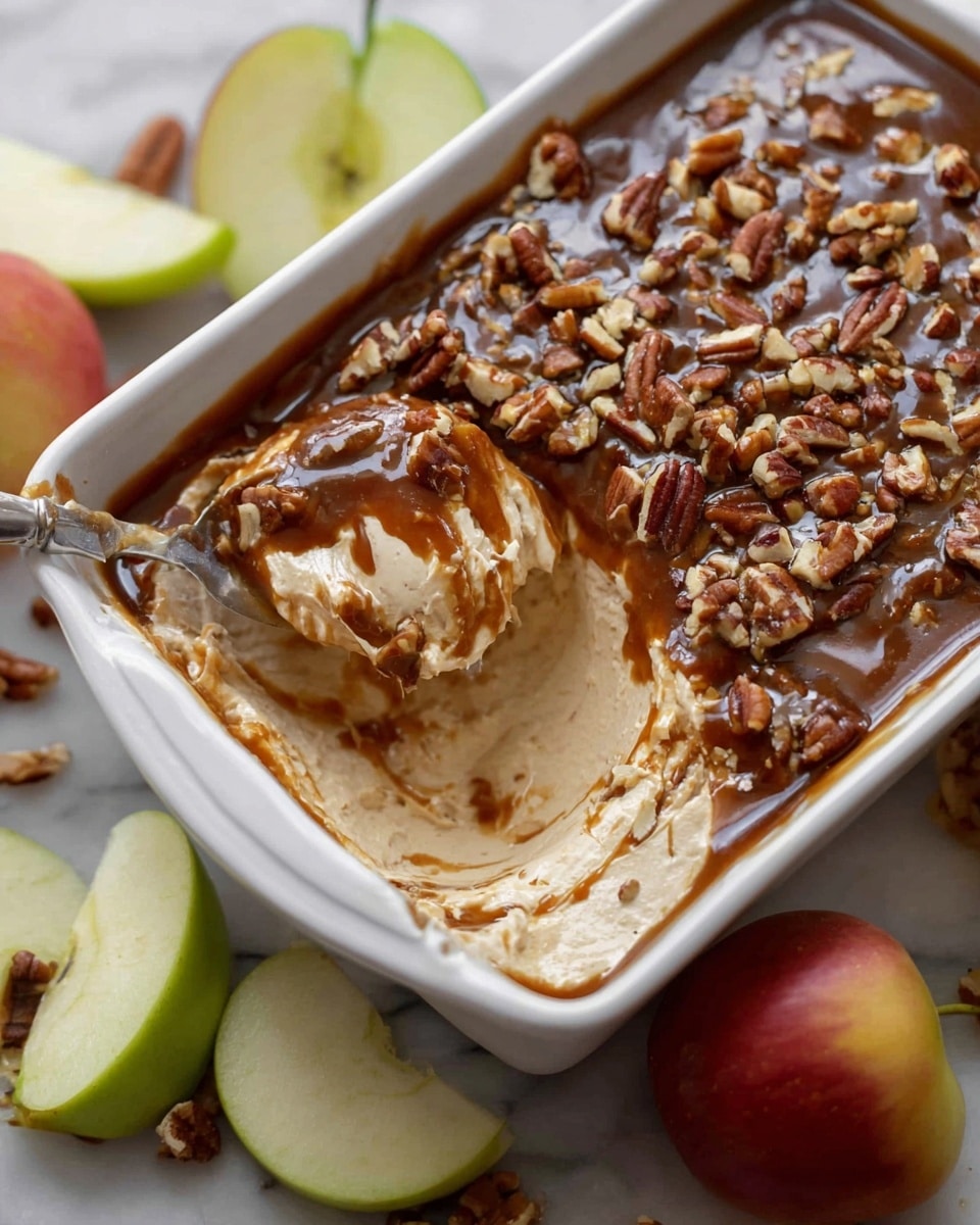A white rectangular dish filled with a creamy dip that has three visible layers; the bottom creamy layer is thick and white, the middle layer is a lighter caramel color mixed inside the creamy layer, and the top layer is a glossy dark brown caramel sauce scattered with chopped pecans. A spoon scoops out some of the dip, showing the mix of creamy and caramel textures. Around the dish are some green and red apple slices on a white marbled surface. Photo taken with an iphone --ar 4:5 --v 7