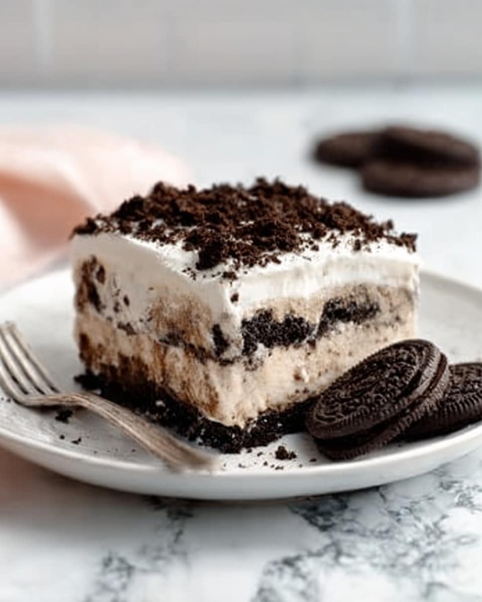 A white plate with a layered dessert that has three distinct layers: a bottom dark crumbly layer resembling crushed cookies, a middle creamy white layer with smooth texture, and a top layer with light brown swirls and white cream. The dessert is topped with crushed dark cookie pieces. A white marbled surface is in the background, with two whole dark cookies leaning against the dessert on the plate and a fork nearby. The lighting is soft and natural, highlighting the textures of the dessert. Photo taken with an iphone --ar 4:5 --v 7