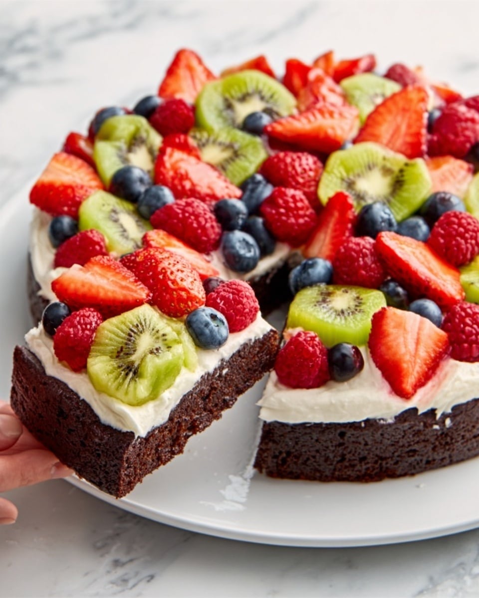 A dark brown chocolate cake base with a moist texture is topped with a thick layer of white cream. On top, there is an even spread of fresh fruit pieces including red strawberries, red raspberries, bright green kiwi slices, and small blue blueberries, arranged close together making the surface colorful and fresh. A woman's hand is gently holding a slice of the cake, showing the layers clearly. The cake sits on a white plate placed over a white marbled surface. The photo taken with an iphone --ar 4:5 --v 7