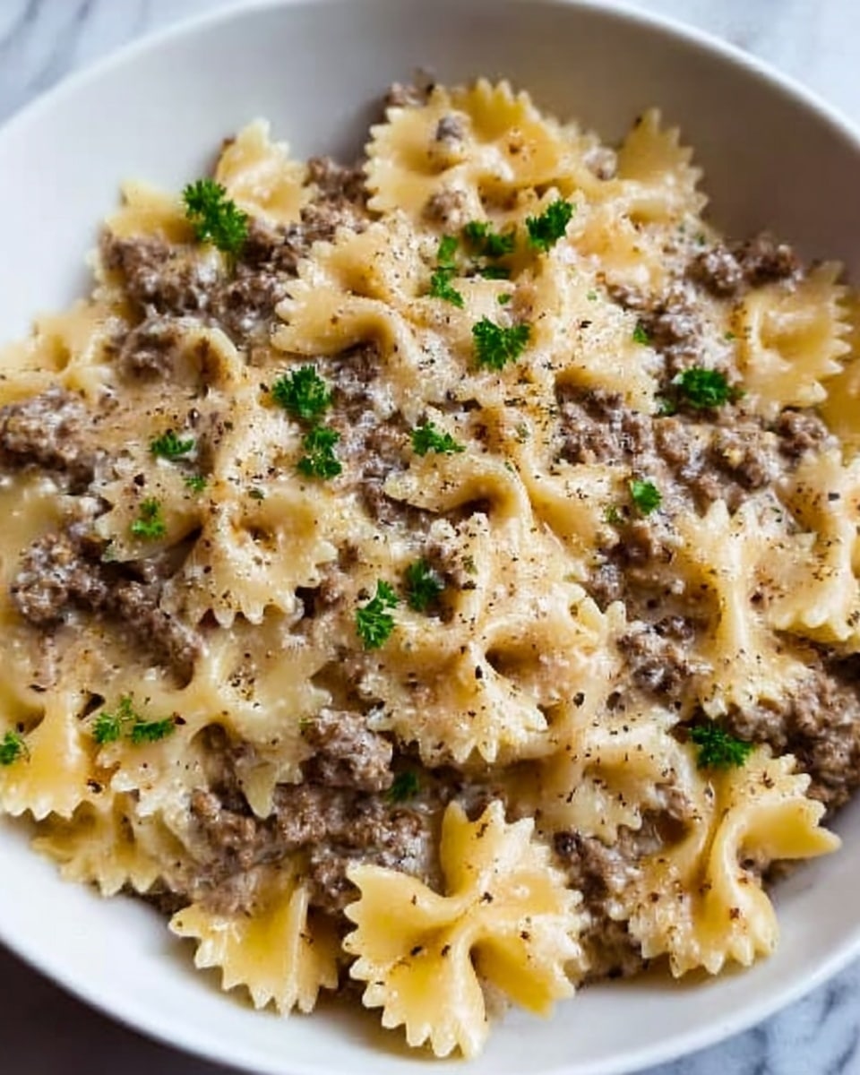 A white bowl filled with farfalle pasta mixed with ground beef in a creamy sauce. The pasta is light yellow with a soft texture, and the ground beef is brown and finely crumbled evenly across the dish. Small green parsley leaves are sprinkled on top, along with a light dusting of black pepper and grated cheese that adds a slight white texture. The creamy sauce coats the pasta and beef, giving the dish a smooth and rich look. The bowl sits on a white marbled surface. Photo taken with an iphone --ar 4:5 --v 7