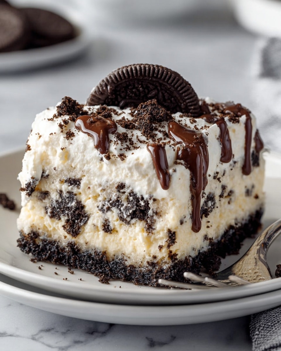 A square piece of cookies and cream dessert sits on a white plate, showing three clear layers: a bottom dark crumb layer made of crushed black cookies, a thick middle white creamy layer with cookie bits mixed in, and a fluffy textured white top layer sprinkled with more cookie crumbs. Thin drizzles of chocolate sauce run vertically over the top, and a whole black sandwich cookie rests right in the center. Crumbled cookie pieces are scattered around the sides, and a silver fork rests on the plate’s edge. The plate is placed on a white marbled surface. photo taken with an iphone --ar 4:5 --v 7